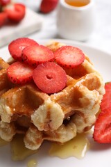 Delicious Belgian waffles with strawberries and honey on plate, closeup
