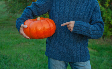 Man in blue sweater holding big orange pumpkin and showing by finger on it