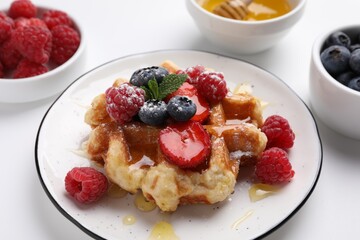 Delicious Belgian waffle with fresh berries and honey on white table, closeup