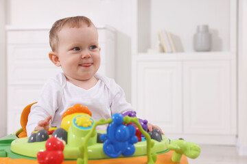 Portrait of cute baby with toy walker at home, space for text. Learning to walk