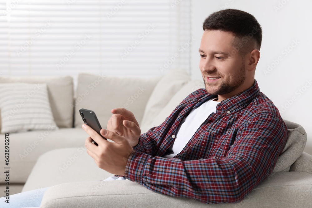 Poster man sending message via smartphone on sofa at home. space for text