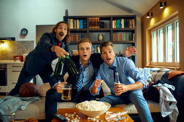 Trio of young businessmen watching a basketball game after work on the couch at home