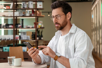 Handsome man sending message via smartphone at table indoors