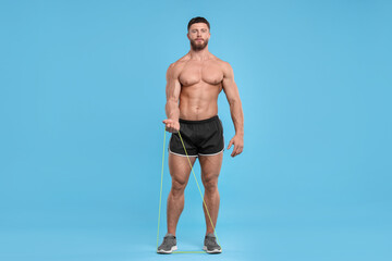 Young man exercising with elastic resistance band on light blue background. Space for text