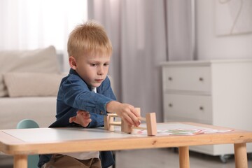 Fototapeta na wymiar Cute little boy playing with wooden toys at table indoors, space for text