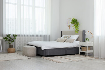 Stylish bedroom interior with large comfortable bed, ottoman and bedside table