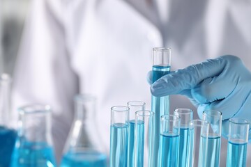 Scientist taking test tube with light blue liquid in laboratory, closeup. Space for text