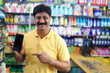 Smiling mid aged man purchasing in a grocery store pointing towards the mobile app. Buying grocery in supermarket pointing towards the mobile app.
