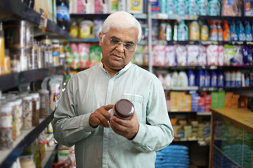 Old man standing in front of product shelf in grocery store. Confused old man buying grocery for...