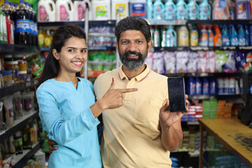 Happy Indian couple enjoying purchasing in grocery store. Buying grocery for home in supermarket. Pointing towards the mobile screen.