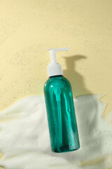 Bottle of face cleanser and white foam on beige background, top view. Skin care cosmetic