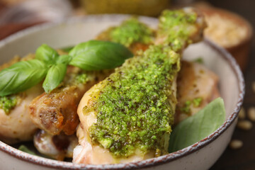 Delicious fried chicken drumsticks with pesto sauce and basil in bowl, closeup
