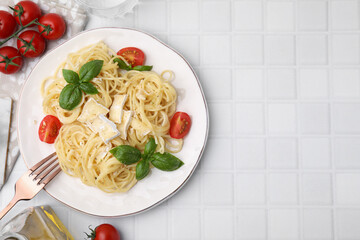 Delicious pasta with brie cheese, tomatoes and basil leaves served on white tiled table, flat lay. Space for text