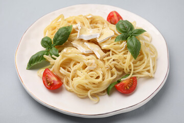 Delicious pasta with brie cheese, tomatoes and basil leaves on grey background, closeup