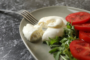 Delicious burrata cheese with tomatoes, arugula and fork on grey table, closeup