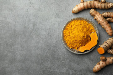 Plate with turmeric powder and raw roots on grey table, flat lay. Space for text