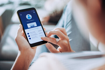Young woman checking the balance of her bank account on a app on the smartphone on the couch at home