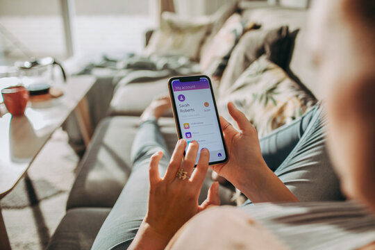 Young woman checking the balance of her bank account on a app on the smartphone on the couch at home