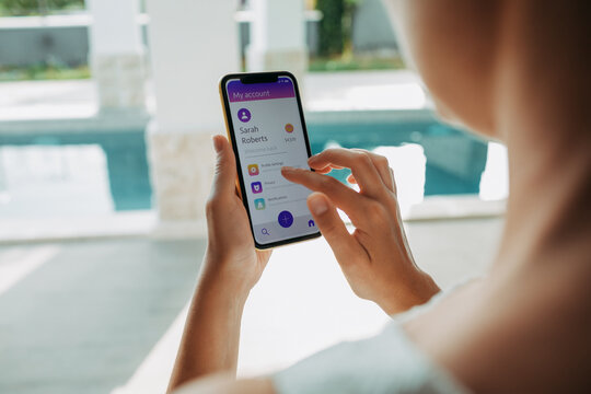 Young woman using a bank app on her smartphone to check her balance while lounging at the pool