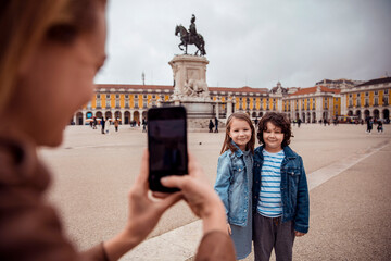 Young children posing for a picture taken by their mother in the Commerce Square in Lisbon