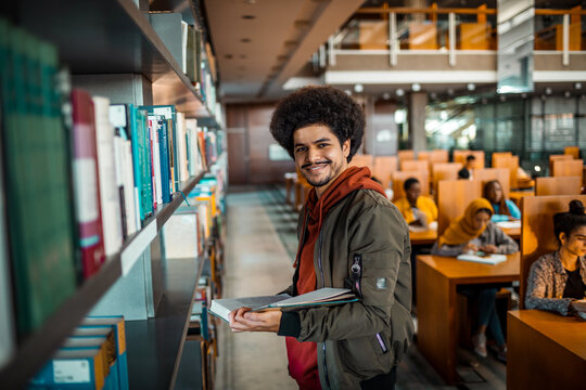 Portrait of a young smart man holding books in a university library