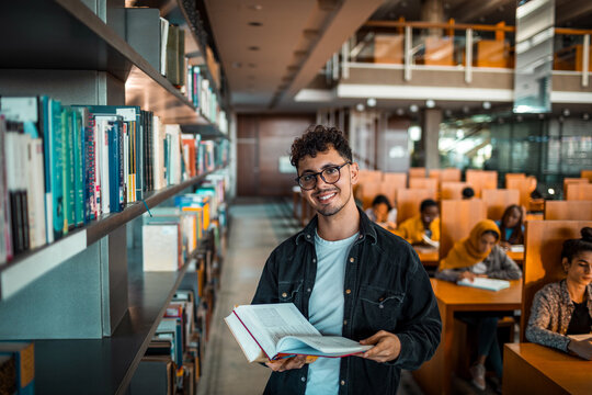 Portrait of a young smart man holding books in a university library