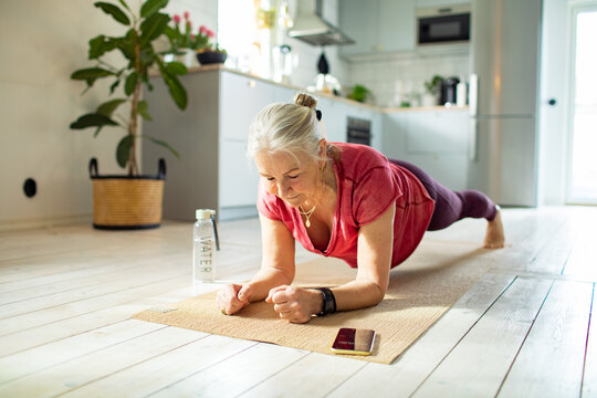 Senior woman doing the plank exercise and timing it on a smartphone at home