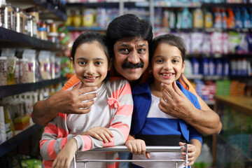 portrait of Indian happy father shopping in a hypermarket with kids, purchasing grocery products as...