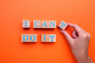 Motivation concept. Woman changing phrase from I Can't Do It into I Can Do It by removing wooden cube with letter T on orange background, top view - obrazy, fototapety, plakaty