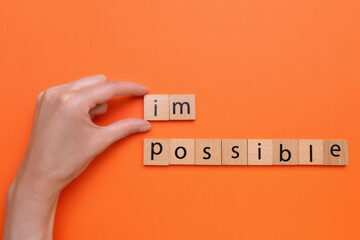 Motivation concept. Woman changing word from Impossible into Possible by removing wooden squares on orange background, top view