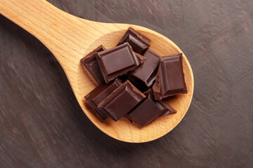 Pieces of dark bitter chocolate in a wooden spoon on a brown wood background