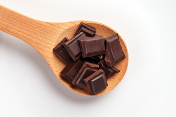 Broken bitter dark chocolate bar with pieces in wooden spoon on white ceramic dish