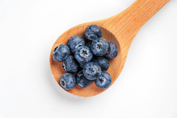 Blueberry fruits in wooden spoon on white ceramic surface. Organic bilberry