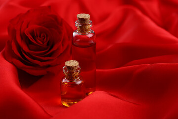 Bottles of love potion and rose flower on red fabric, space for text