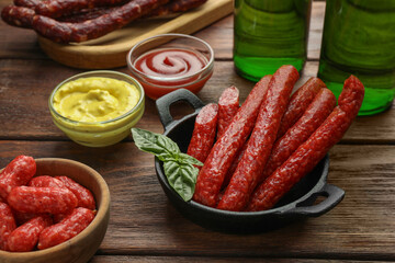 Thin dry smoked sausages, basil and sauces on wooden table