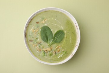 Delicious broccoli cream soup with basil and pumpkin seeds on green background, top view