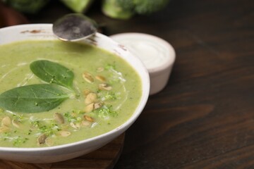 Delicious broccoli cream soup with basil and pumpkin seeds served on wooden table, closeup. Space for text