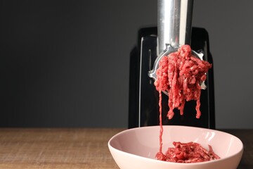 Electric meat grinder with beef mince on wooden table against grey background, closeup. Space for...