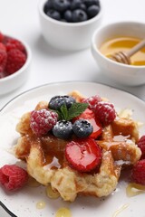 Delicious Belgian waffle with fresh berries and honey on white table, closeup