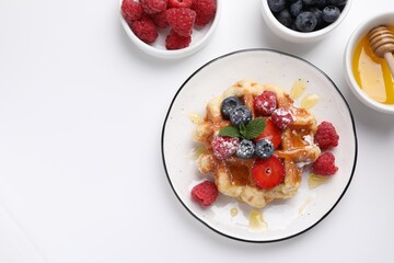 Delicious Belgian waffle with fresh berries and honey on white table, flat lay. Space for text