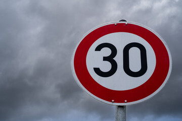 Round speed sign 30 kilometers per hour with cloudy sky in the background - obrazy, fototapety, plakaty