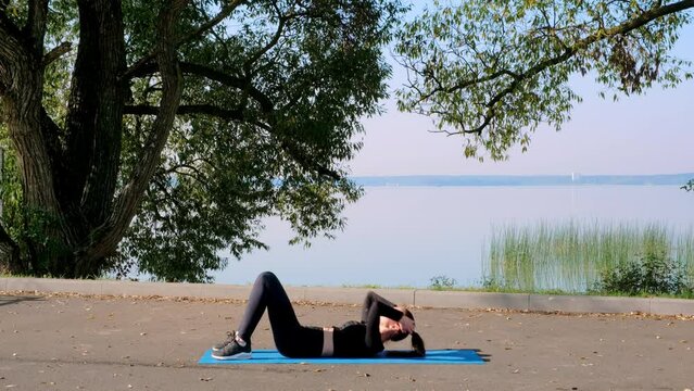 Slim 30s woman in black sportswear practices pilates doing bridge exercise, backbend pitha asana in nature. Fitness training for firm buttocks. Strong healthy body. Hatha practicing. Sport blogging. 