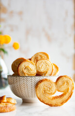 Puff pastry palmiers in a bowl on a white marble table. Homemade bakery for breakfast. Vertical picture.