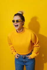 Young cheerful girl wearing yellow sweatshirt and sunglasses against yellow background