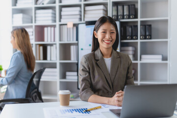 Beautiful Asian businesswoman sitting smiling and happy  with laptop computer in the office. Looking at camera.