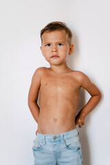 Cute little boy wearing blue jeans posing against white background with silly facial expression