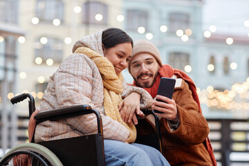 Portrait of young woman with disability taking selfie photo outdoors with boyfriend and using...