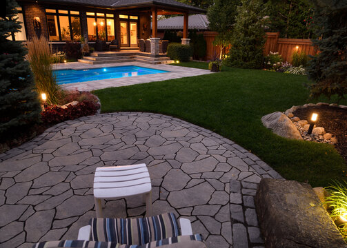 House with outdoor patio sitting area and lights on at night and blue lit swimming pool with stone deck