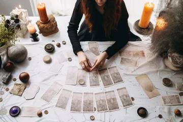 Poster a close up of female hands drawing the tarot cards from the deck. A fortune teller woman with tattoos doing divination indoors, white and black color palette © Romana