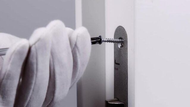 A handyman in white gloves repairs the lock on the door. close-up of a worker's hands installing a new door lock.